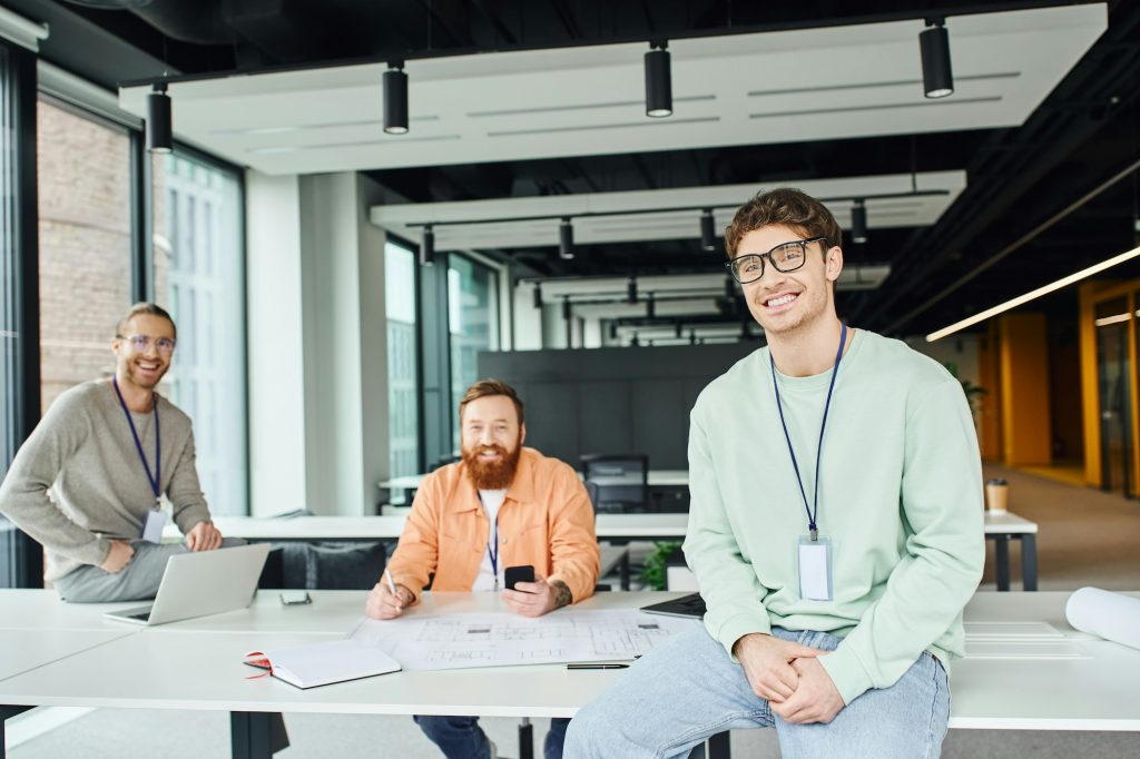happy team lead in eyeglasses looking at camera near smiling architects working on startup project